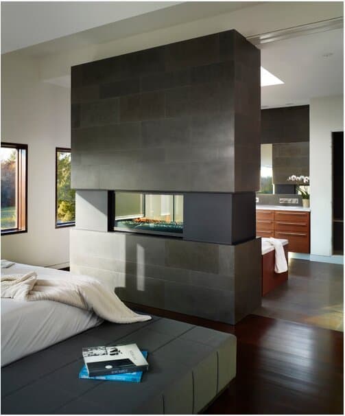 Stone-clad two-sided fireplace wall dividing a bedroom and ensuite bathroom