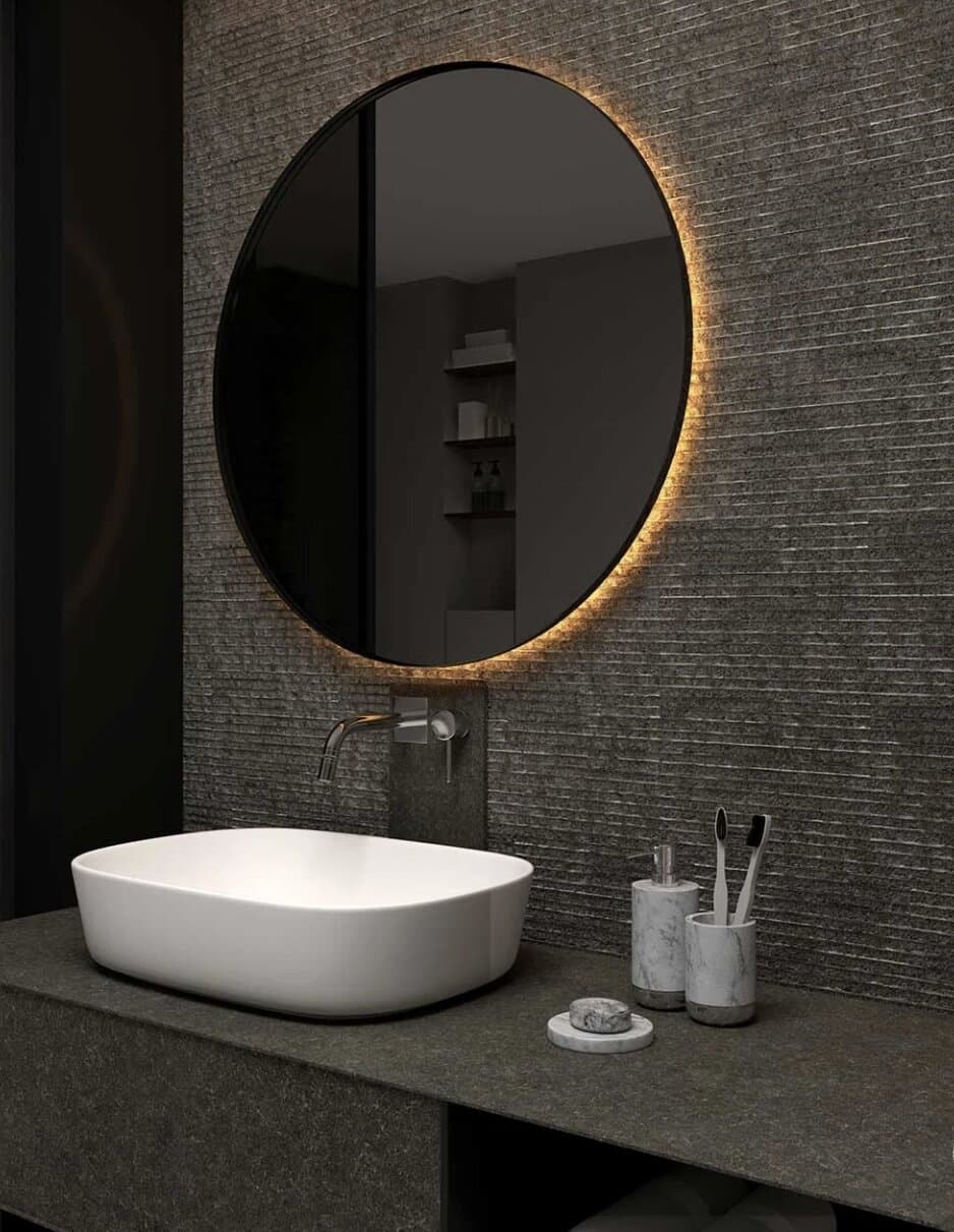 Ribbed textured stone wall panel behind a bathroom vanity with a round backlit mirror
